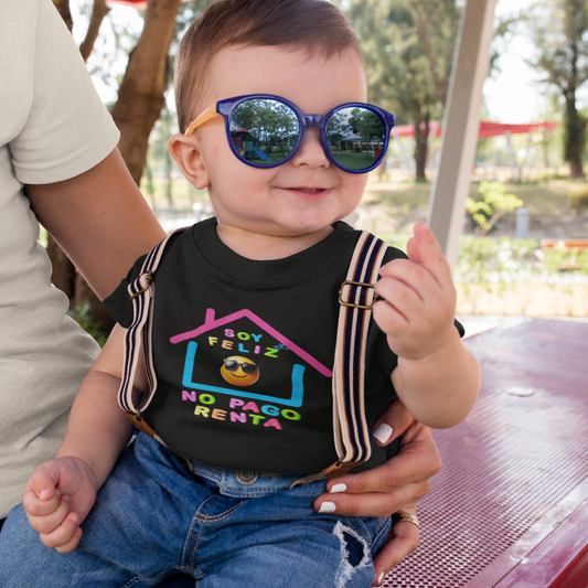 Baby wearing colorful sunglasses and a black shirt with text, sitting in a park.

